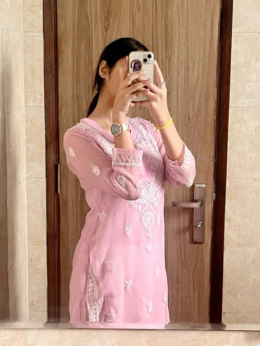 A woman wearing a baby pink georgette chikankari kurti with floral embroidery, taking a mirror selfie.
