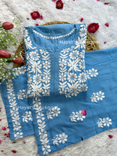 Powder blue chikankari rayon kurta set with intricate white floral embroidery, displayed on a white fur background with decorative red rose petals and artificial tulips. The set is from Hayat&