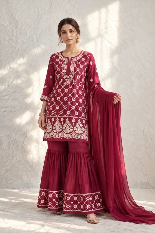 A woman wear a deep maroon and plum shade three-piece traditional kurta garara outfit with intricate cream embroidery of chikankari featuring a kurta, flared sharara pants, and a matching dupatta. Hayat's Lucknowi
